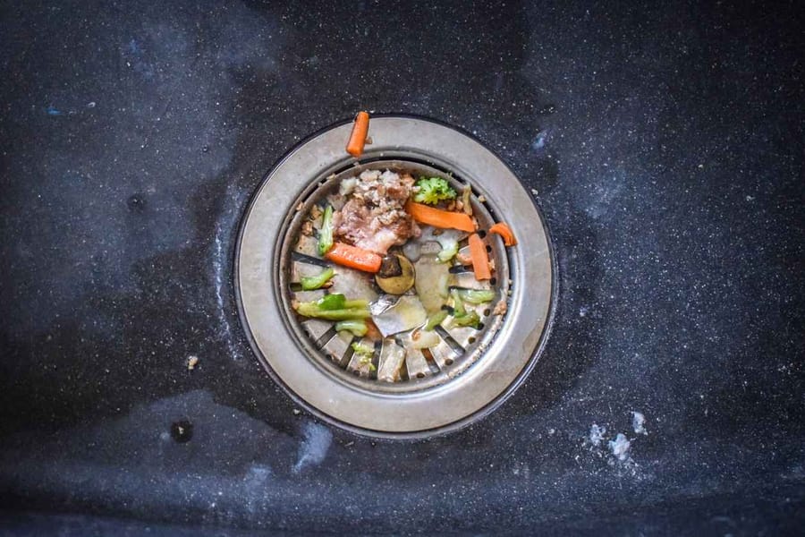 A dirty sink with leftover food bits that clog up the flow of water.