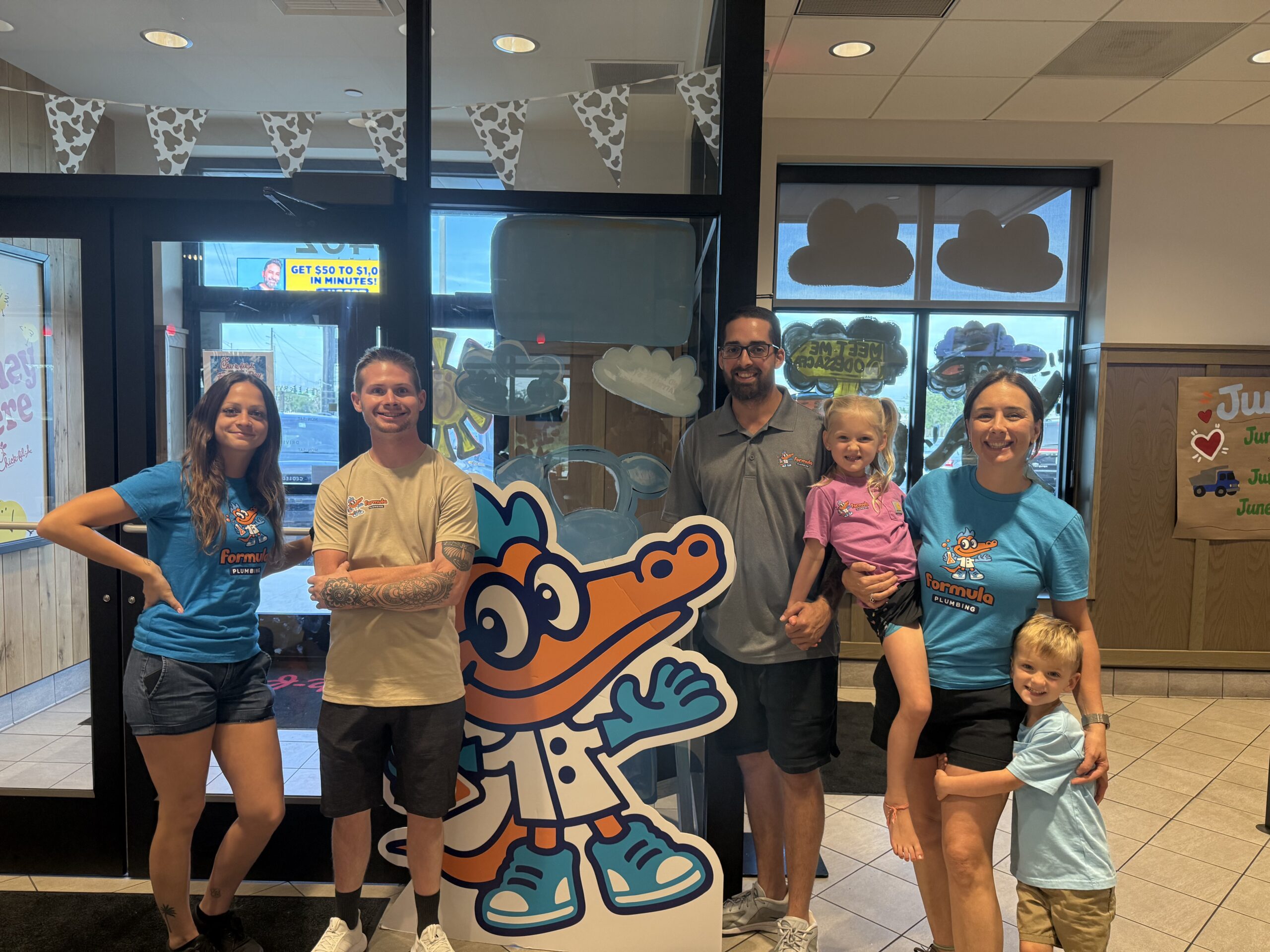 Formula Plumbing team members and a family posing with the company alligator mascot cutout