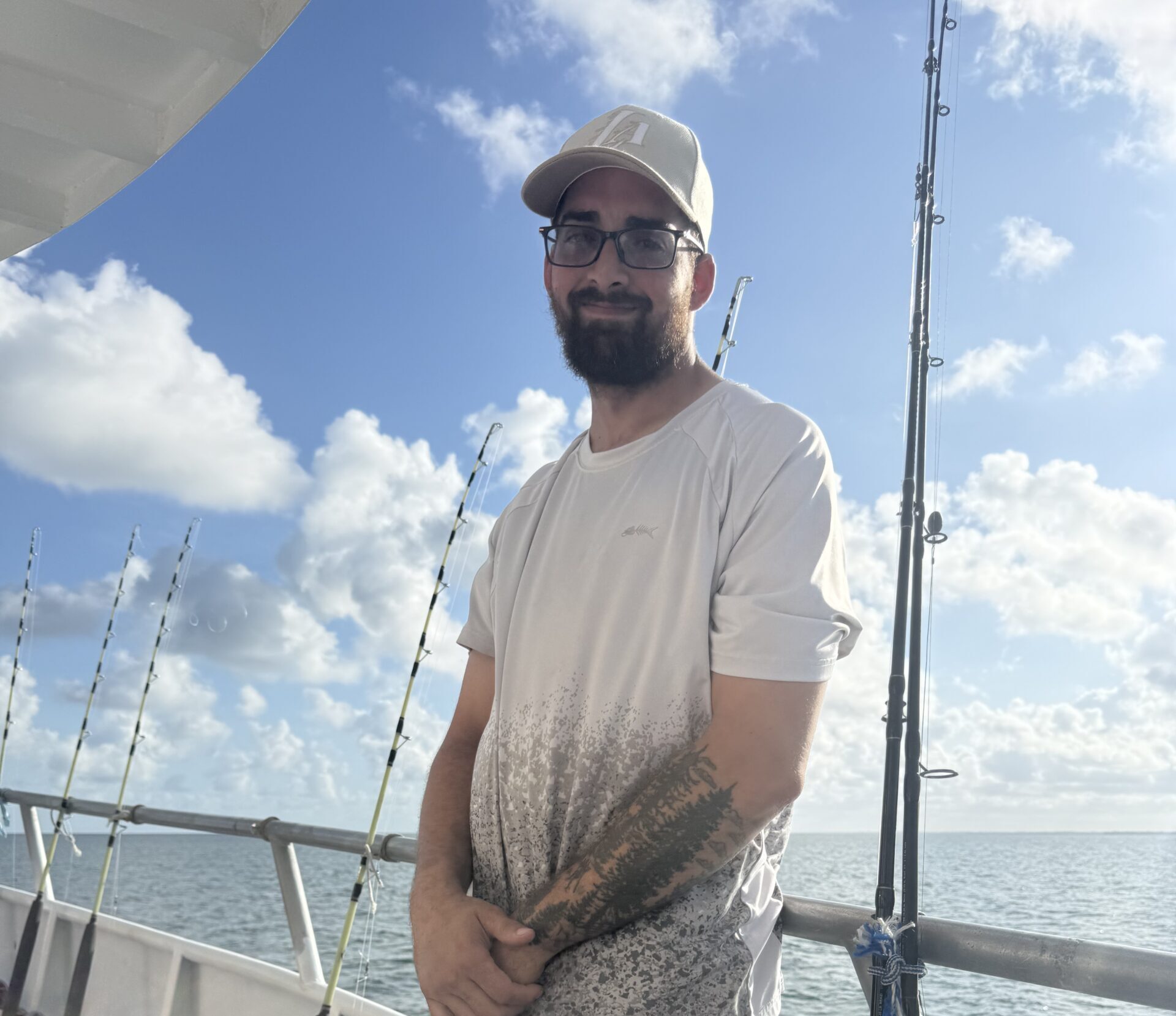 A man in a hat and fishing shirt standing on the deck of a charter boat beside a row of fishing rods