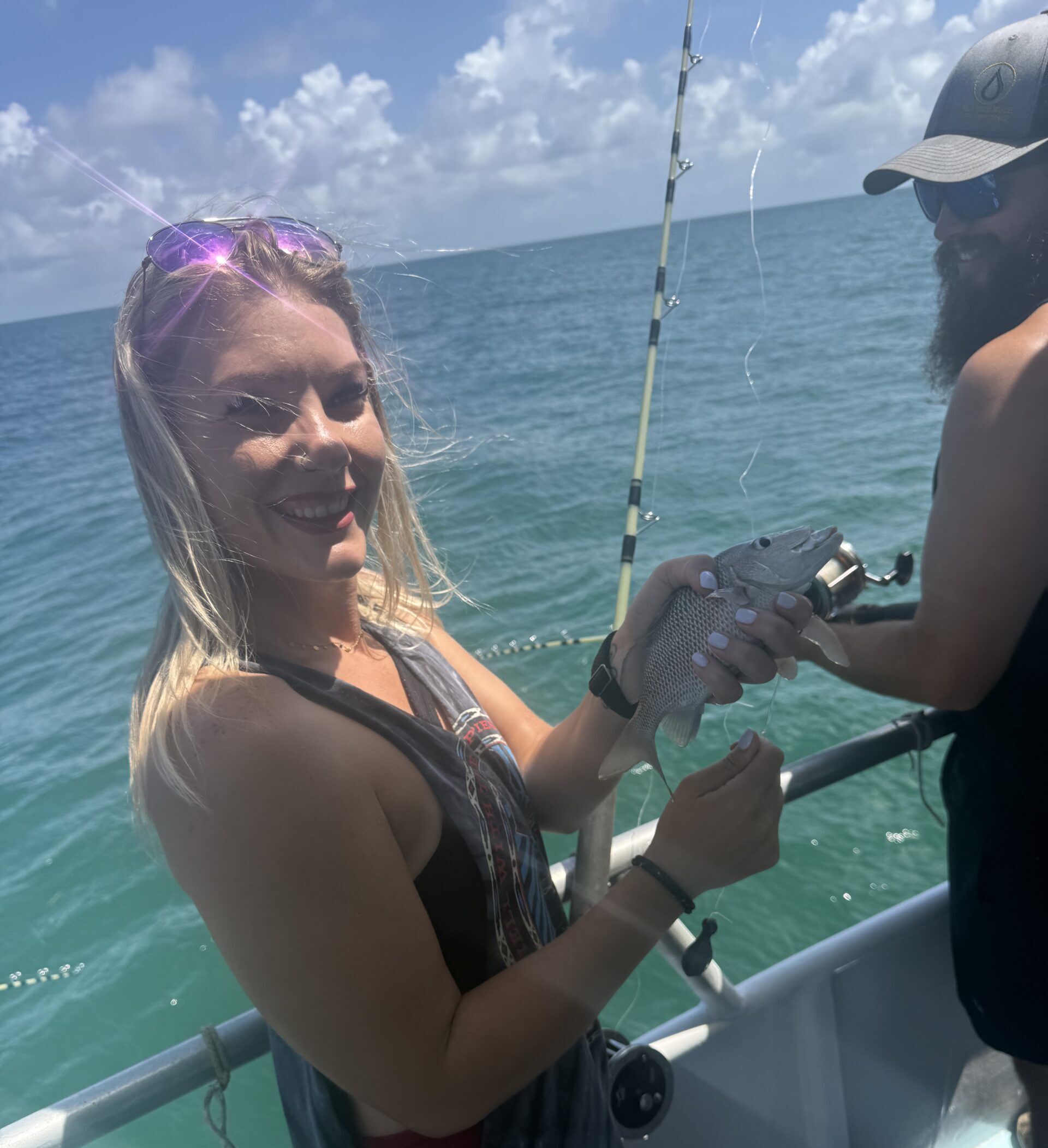 A smiling woman on a charter boat holding a fish she caught, with the ocean behind her