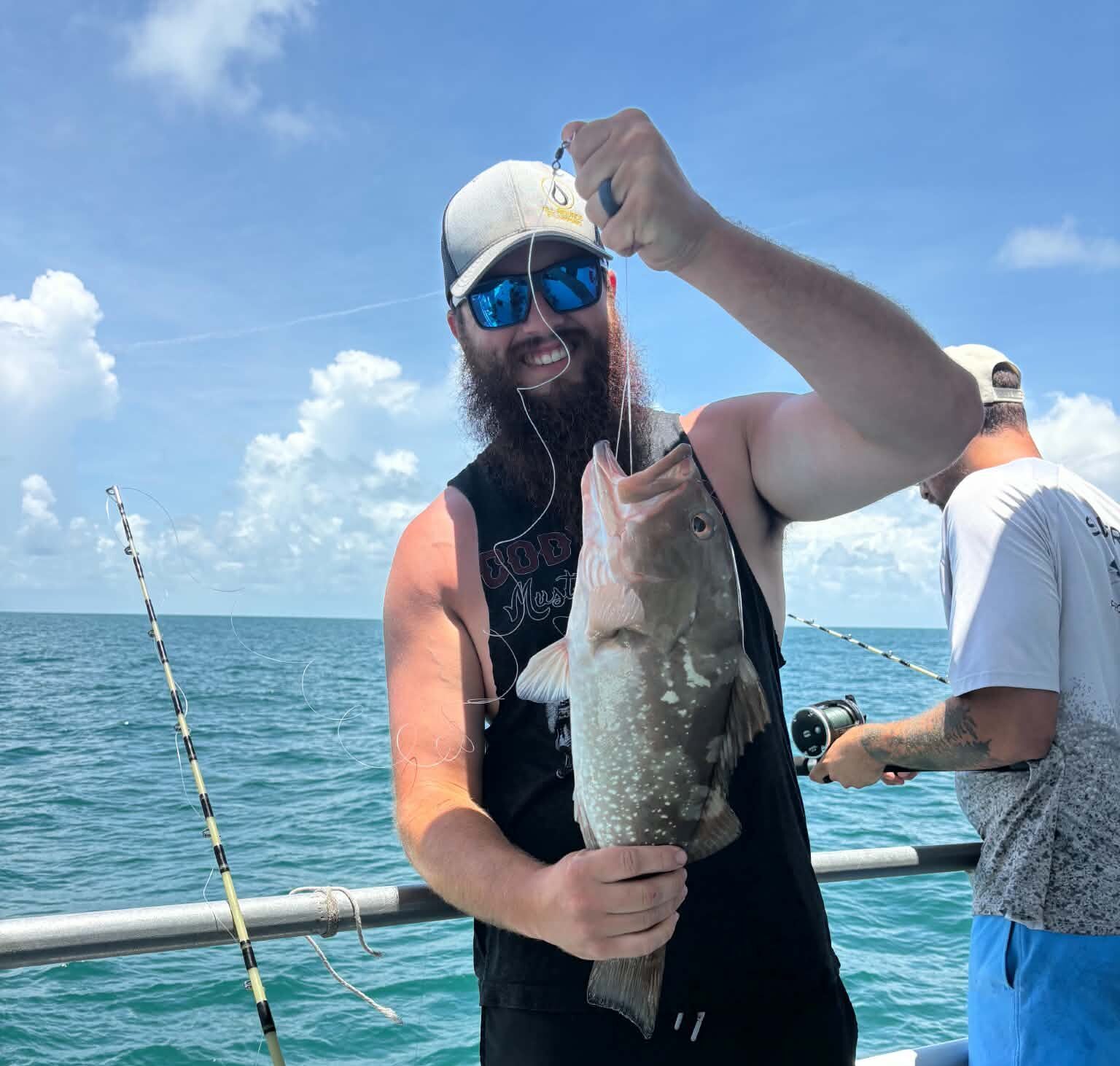Bearded man in a cap and mirrored sunglasses on a boat holding a large fish.