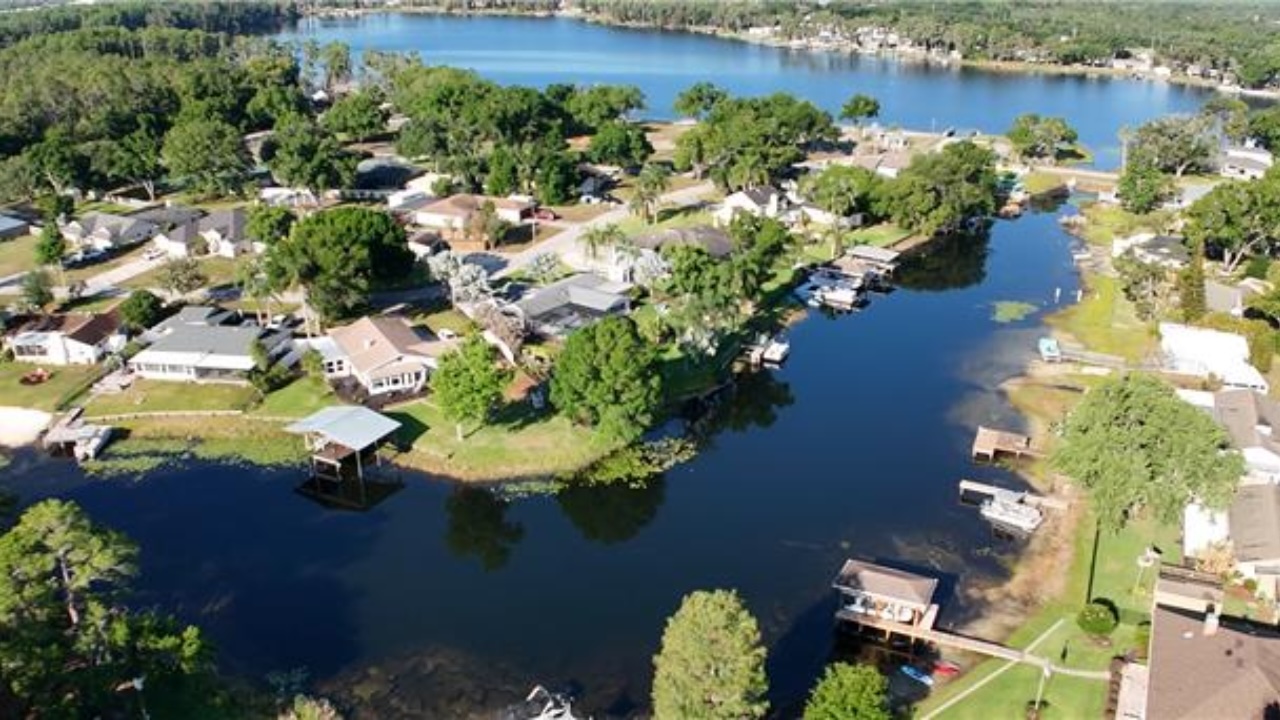 Aerial view of a lakeside neighborhood with houses, trees, and several boat docks along a calm waterway.