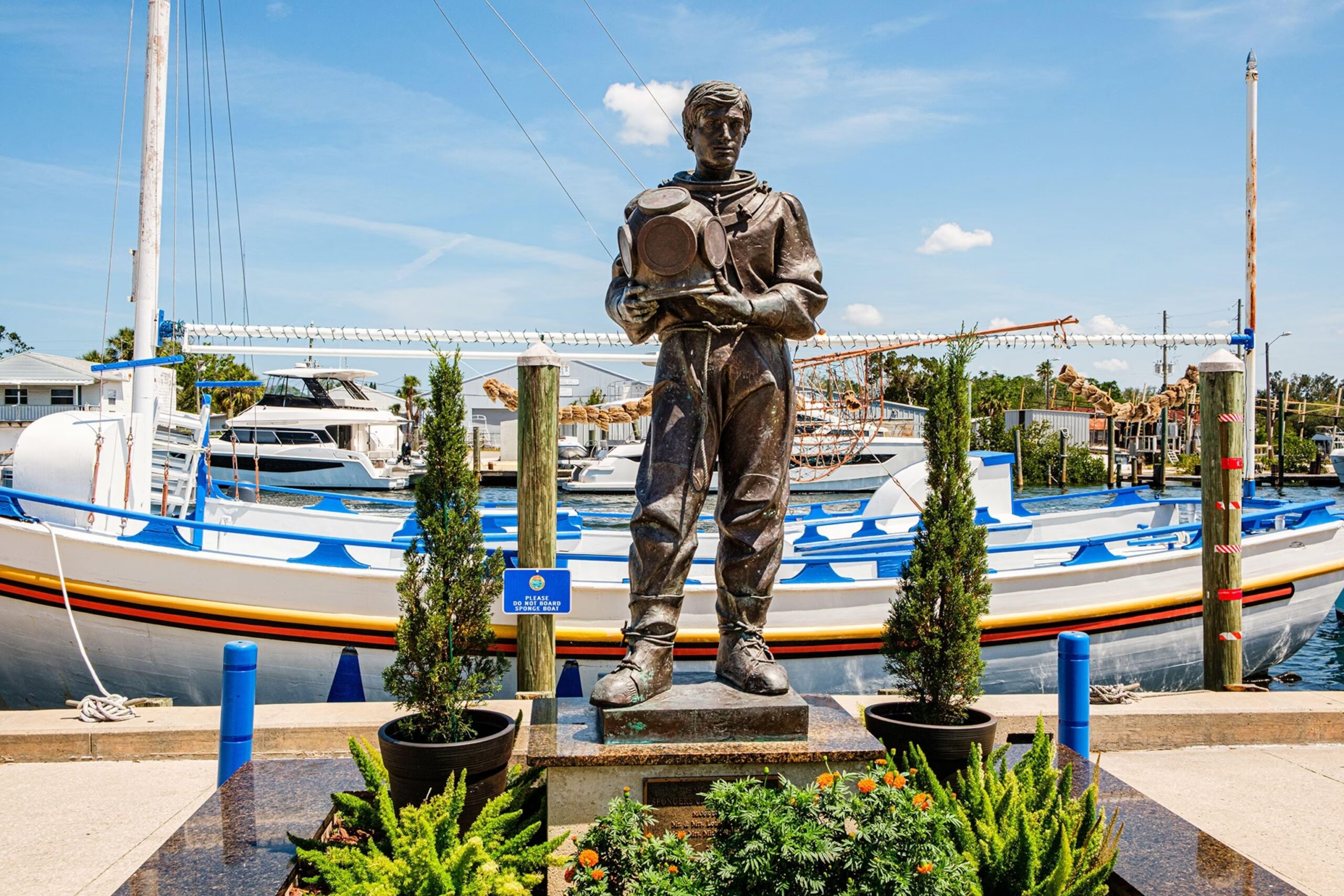Bronze statue of a sponge diver at a marina, with boats docked behind it.
